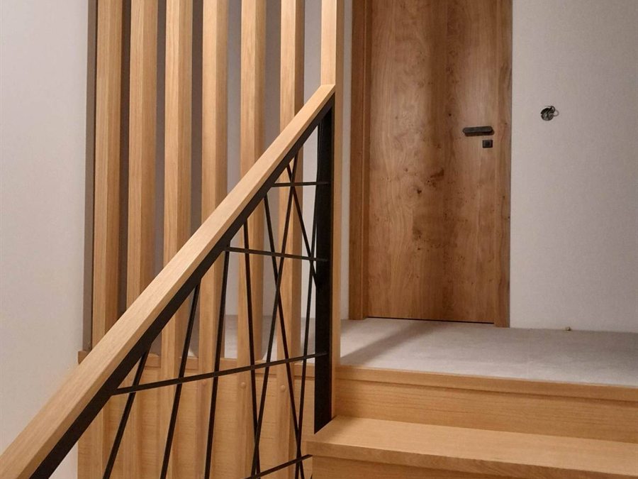 Obklad betonového schodiště dubovými stupni s kovovým zábradlím a dřevěnou lamelovou stěnou